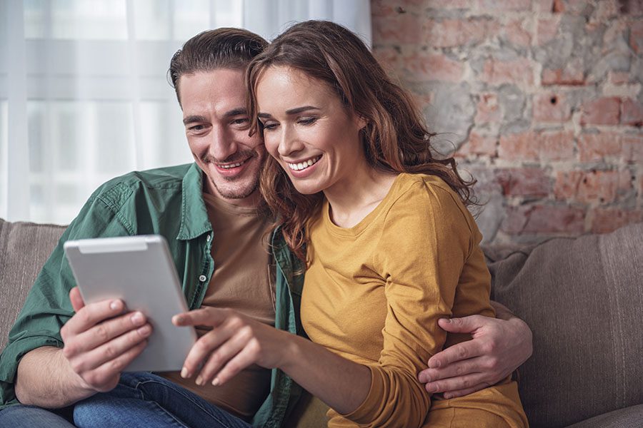 Client Center - Portrait of a Smiling Married Couple Sitting on the Sofa While Using a Tablet Together