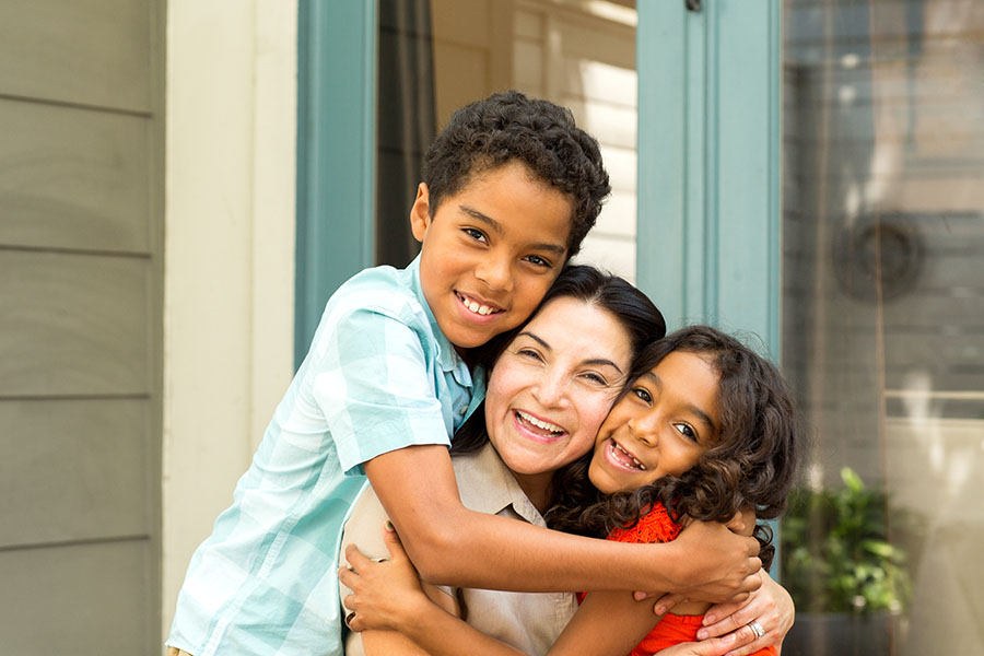Personal Insurance - Closeup Portrait of Two Kids Hugging Their Happy Mother Outside the Front Door of Their Home